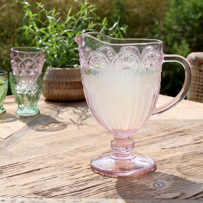 Spangles Fleur embossed glass jug in dusty pink, filled with a pale drink and placed on a wooden outdoor table.
