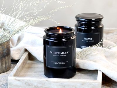Lucon Scented Candle - White Musk - White Candle in Dark Glass Container.  Black Label with White Writing.  shown lit