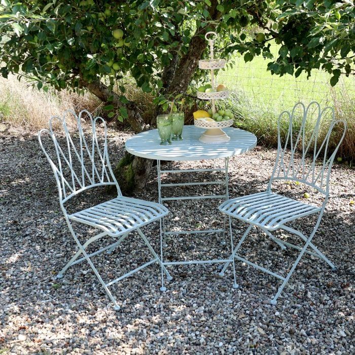 Folding metal bistro set with two decorative chairs and a round table, featuring curved detailing and a light, airy design.