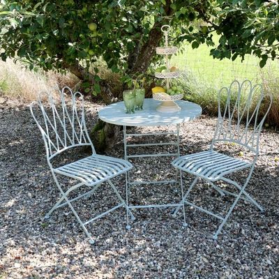 Folding metal bistro set with two decorative chairs and a round table, featuring curved detailing and a light, airy design.