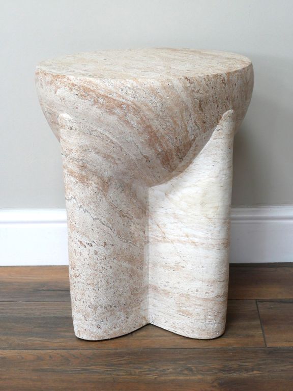 Sculptural stone-effect side table with curved pillar legs and a travertine-style finish in soft natural cream tones.