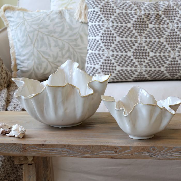 White ceramic bowl shaped like a seashell with gold-edged rim, styled on a table in a coastal-inspired interior.