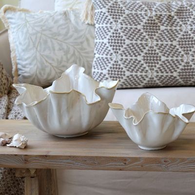 White ceramic bowl shaped like a seashell with gold-edged rim, styled on a table in a coastal-inspired interior.