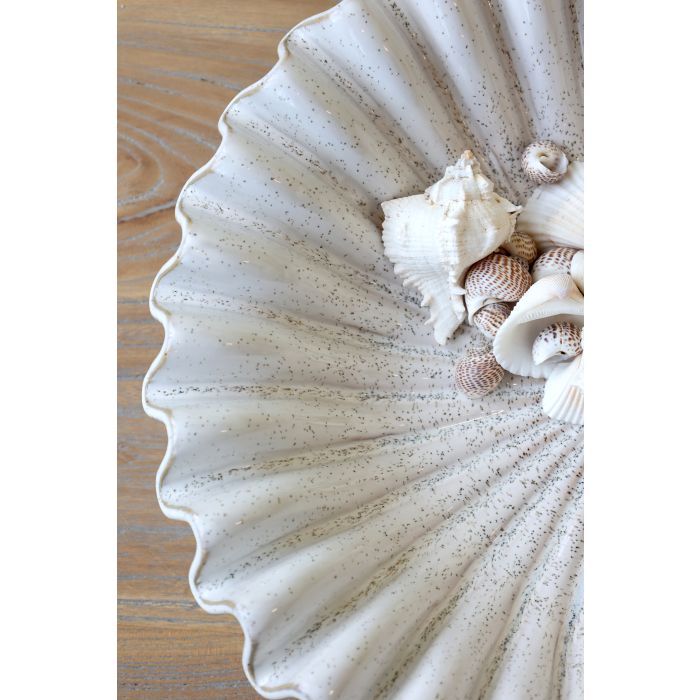 Large white ceramic shell bowl with scalloped edges, filled with seashells and displayed on a wooden coffee table.