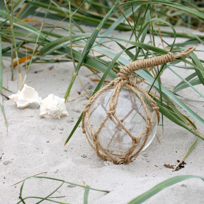 Decorative clear glass fishing float wrapped in natural rope netting, perfect for coastal and nautical home décor.