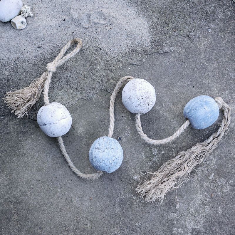 Weathered blue and white wooden fishing floats threaded on natural rope with tassels, styled on a rustic surface.