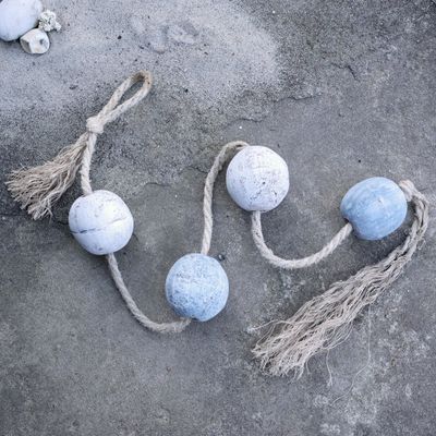 Weathered blue and white wooden fishing floats threaded on natural rope with tassels, styled on a rustic surface.
