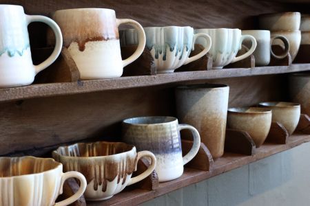 Amelie horizontal wooden compartment shelf displaying handcrafted ceramic mugs, bowls and cups in a warm rustic interior.