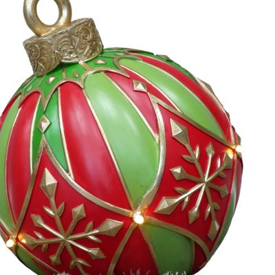 Grand Snowflake Light-Up Christmas Display Bauble Oversized red and green Christmas display bauble with gold snowflakes and warm lights, arranged beside a festive tree.