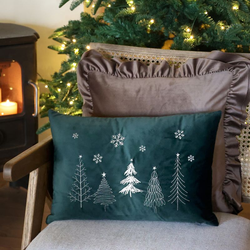 Deep green rectangular cushion embroidered with cream Christmas trees and scattered snowflakes.
