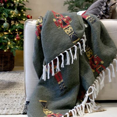 Forest-green woven Christmas throw with red nutcracker guards and an ivory knotted fringe.