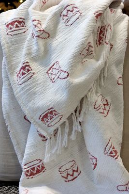 Textured ivory Christmas throw patterned with small red toy drums and finished with a soft fringed edge.