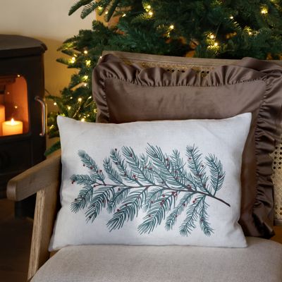 Natural rectangular cushion printed with a sweeping dark green evergreen branch and scattered red winter berries.