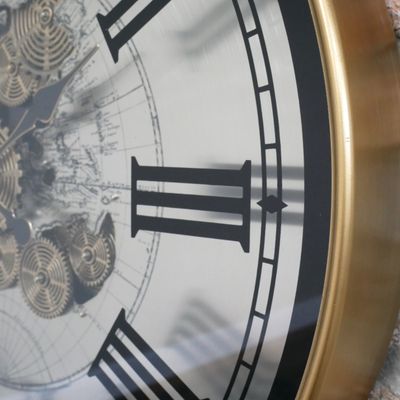 Extra-large round clock with an antique-brass frame, Roman numerals, a world map and decorative central cogs.
