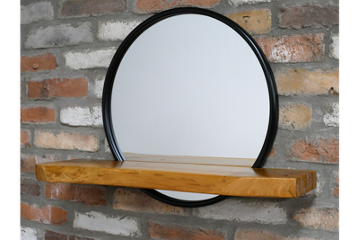 Circular black-framed wall mirror with a natural wood shelf, combining simple style with practical display space.