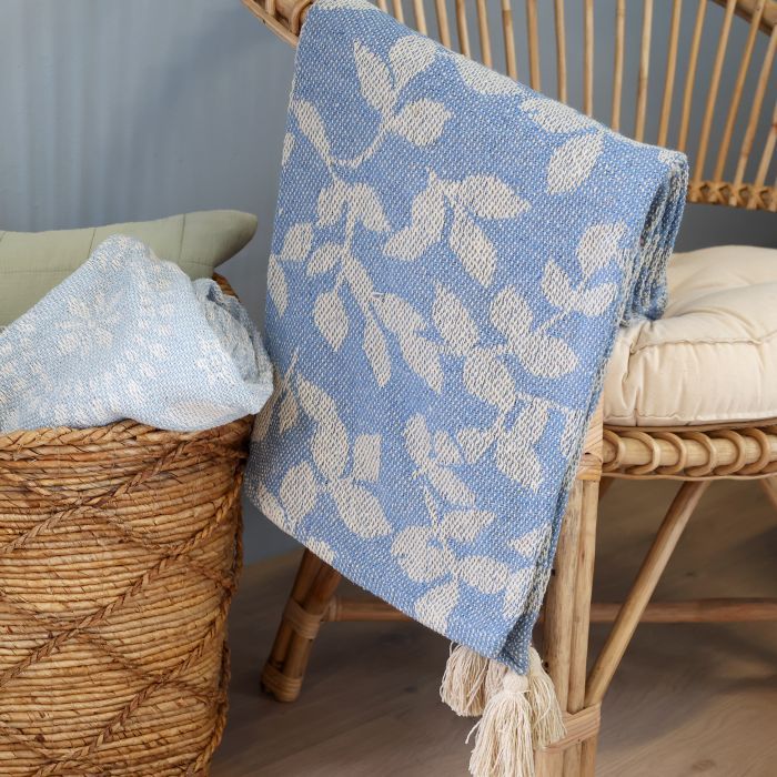 Blue woven throw featuring an ivory leaf and vine pattern, textured finish and decorative cream tassels at the corners.