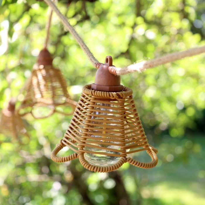 Natural rattan bell-shaped garden string lights with open woven shades, visible bulbs and rope-style cable hanging in a tree.