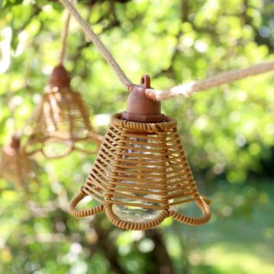 Natural rattan bell-shaped garden string lights with open woven shades, visible bulbs and rope-style cable hanging in a tree.