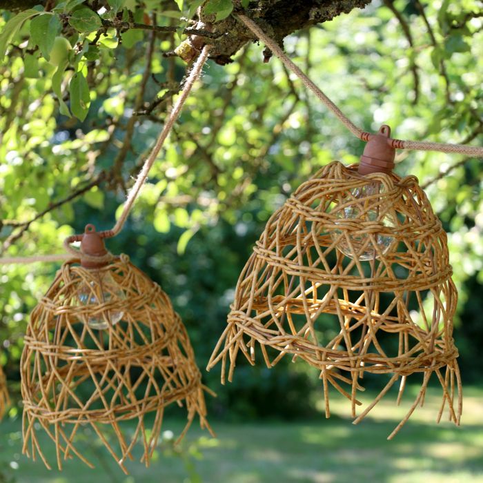 Rustic woven willow garden lanterns with open latticework, bell-shaped designs and hanging ropes suspended from a tree.