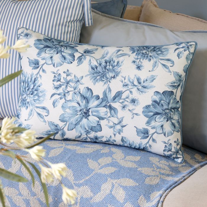 Rectangular ivory cushion featuring delicate blue floral blooms, trailing leaves and stems, finished with blue piped edges.