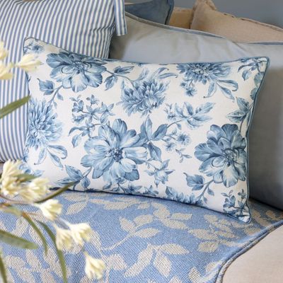 Rectangular ivory cushion featuring delicate blue floral blooms, trailing leaves and stems, finished with blue piped edges.