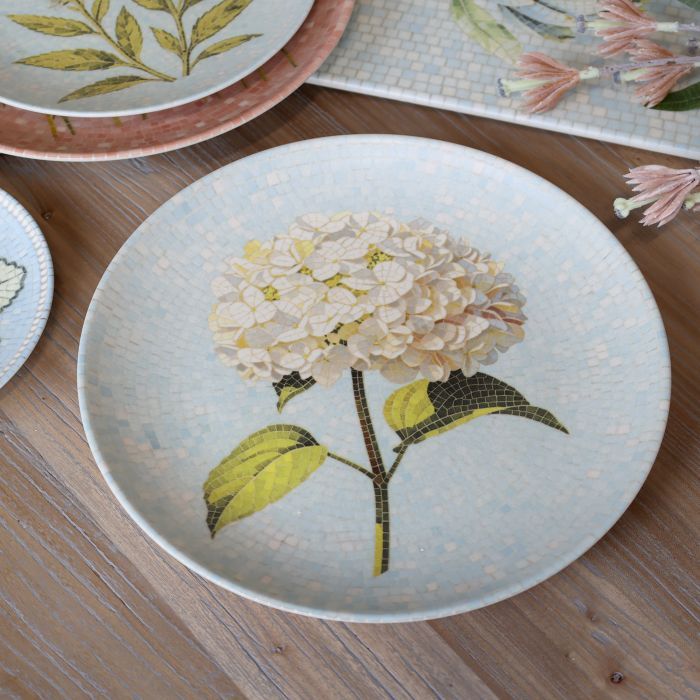 Round Chartres mosaic tray with an ivory hydrangea flower, green leaves and delicate pale blue and cream tiled background.