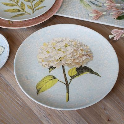 Round Chartres mosaic tray with an ivory hydrangea flower, green leaves and delicate pale blue and cream tiled background.