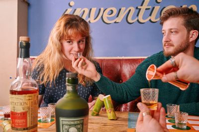 Rum Making Masterclasses at the Brewhouse and Kitchen "A woman tasting rum from a shot glass while a man looks on, during a rum tasting masterclass. Bottles of rum and other tasting materials are on the table."