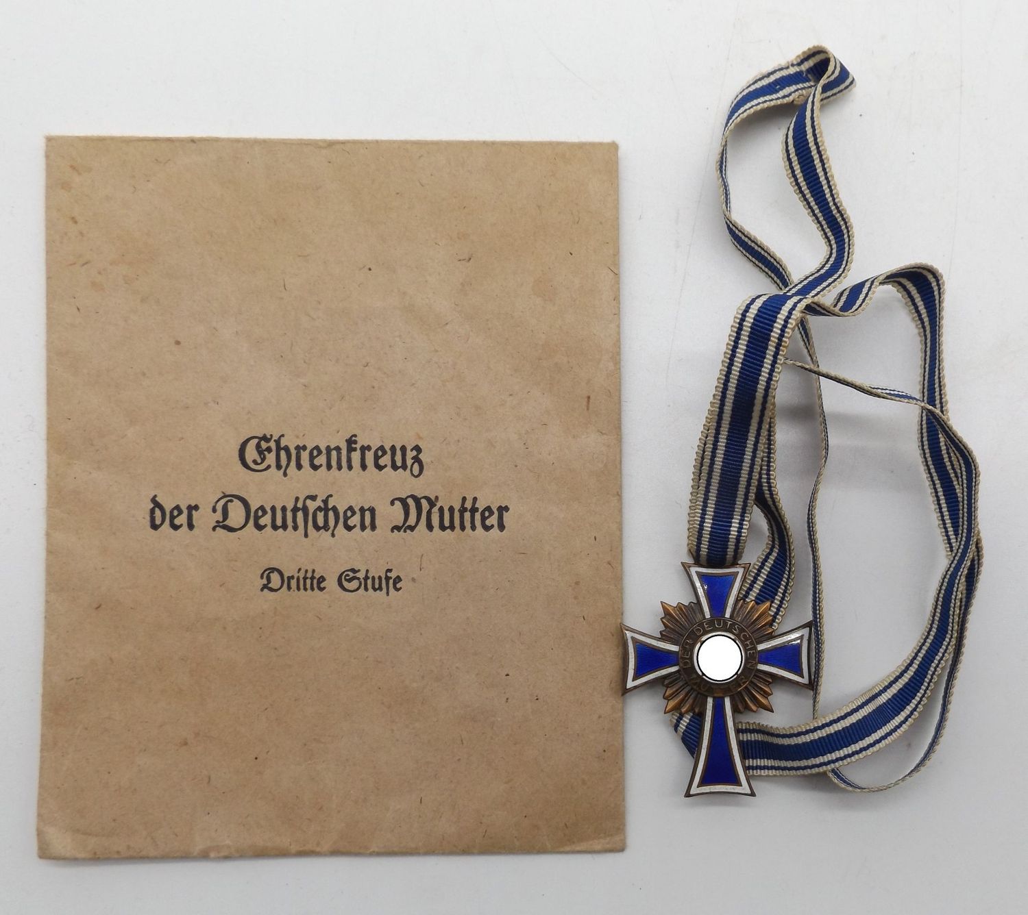 Mutterkreuz in Bronze, 3. Stufe, am konfektionierten langen Band, Emaille vollständig erhalten mit Verleihungstüte Frank & Reif, Stuttgart.