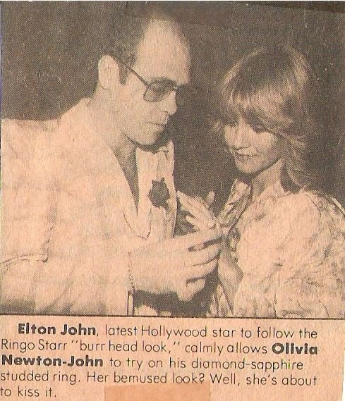 John, Elton / With Olivia Newton-John, Putting Ring On Her Finger | Magazine Photo with Caption (1976)