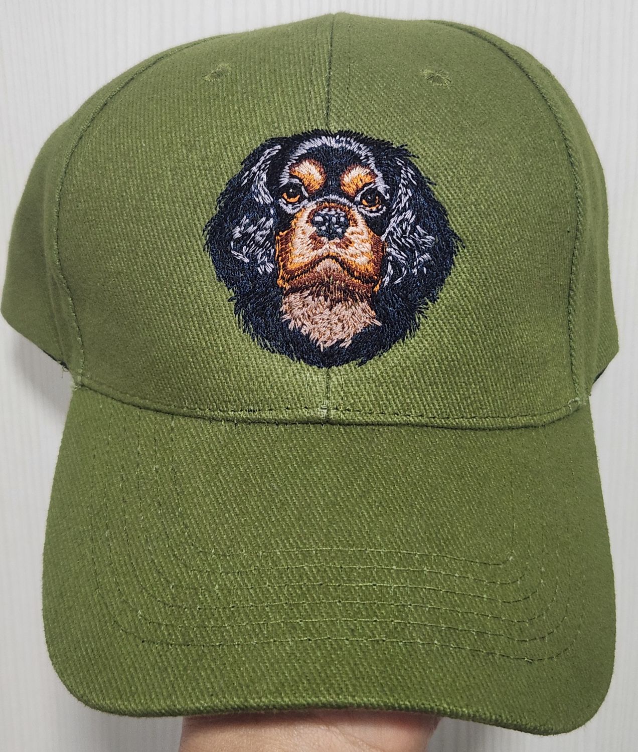 Olive green baseball cap featuring a detailed custom embroidered head of a black and tan Cavalier King Charles Spaniel dog.