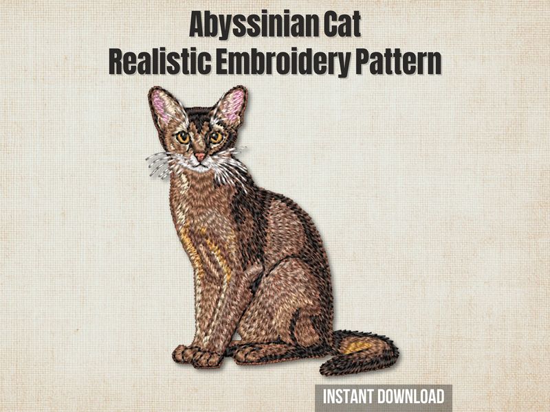 Embroidery of an Abyssinian cat in golden‑brown and cream thread with detailed fur texture and on a light fabric background.