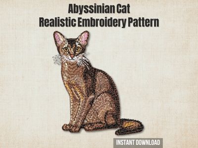Embroidery of an Abyssinian cat in golden‑brown and cream thread with detailed fur texture and on a light fabric background.