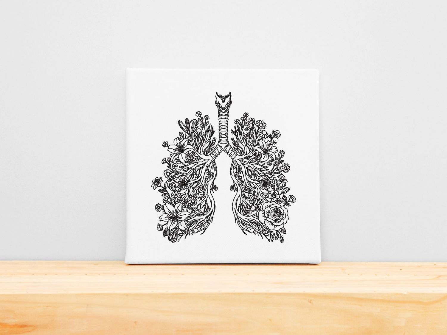 High-precision embroidery of anatomical lungs blooming with various wildflowers on a white stretched canvas frame.