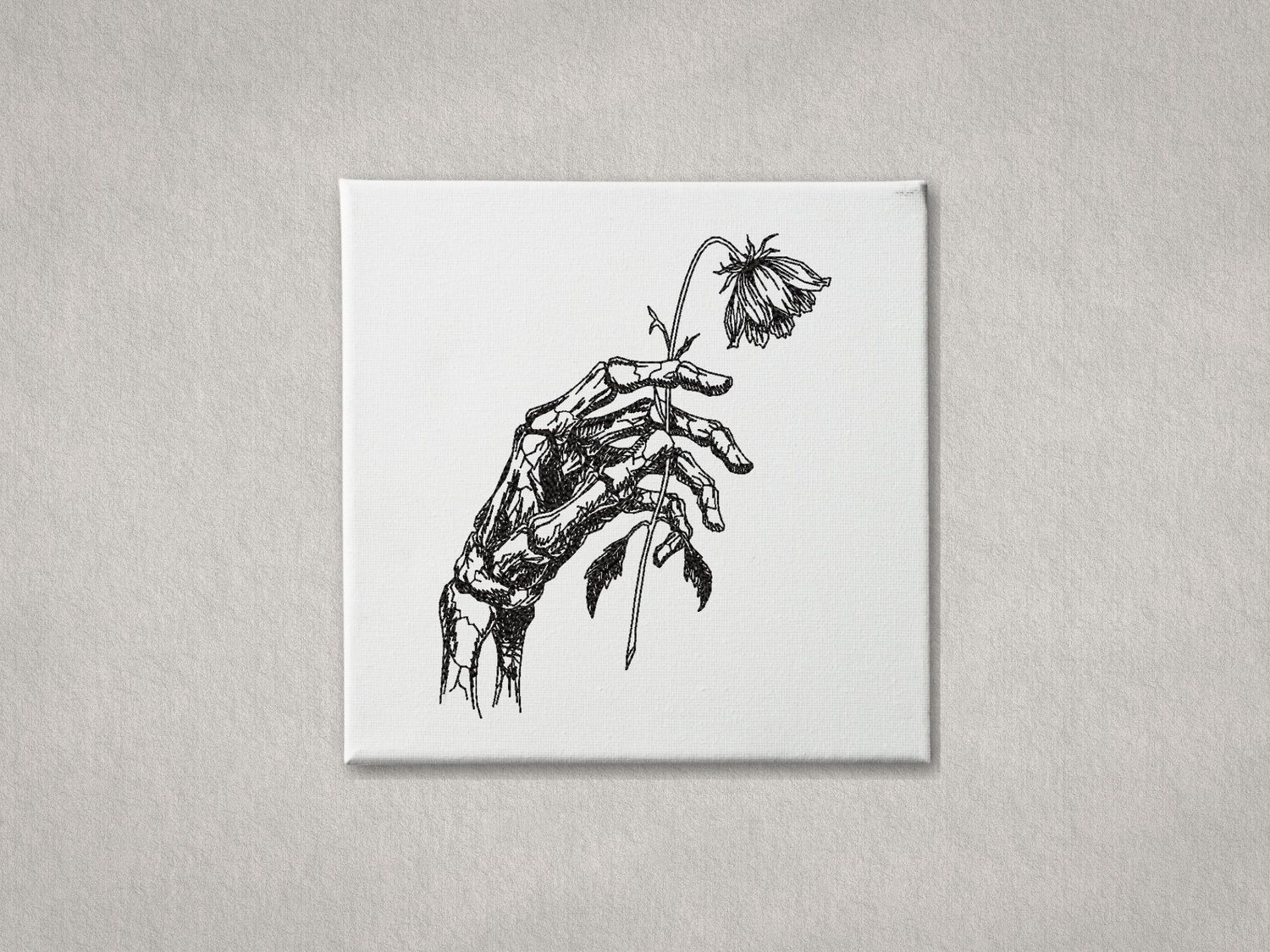 Black embroidered skeletal hand holding a wilted flower on white gallery-wrapped canvas. Minimalist grey wall background.
