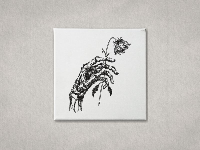 Black embroidered skeletal hand holding a wilted flower on white gallery-wrapped canvas. Minimalist grey wall background.