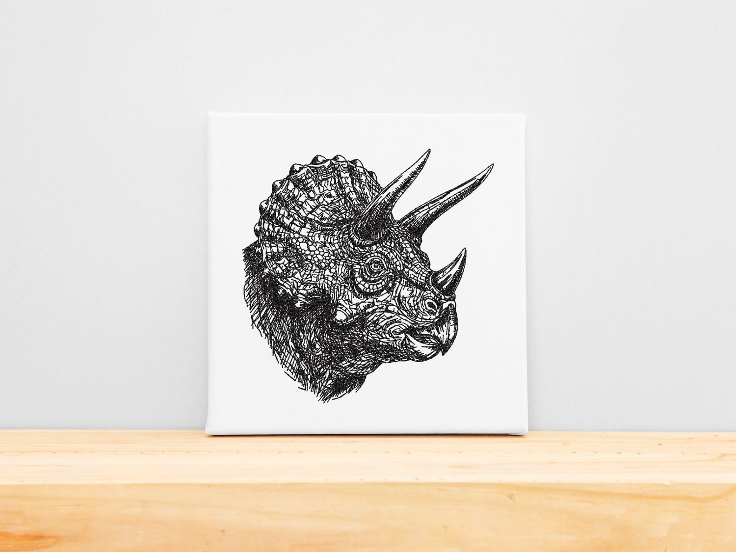 High-precision black machine embroidery of a detailed Triceratops head on a white stretched canvas frame.