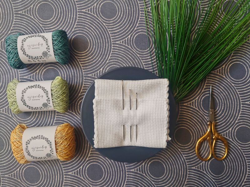 Was ist Sashiko? - Japanische Stickerei links - japanische Sashiko-Stickgarne, im HIntergrund japanischer Stoff, in der MitteSashiko-Sticknadeln, rechts -Stickschere