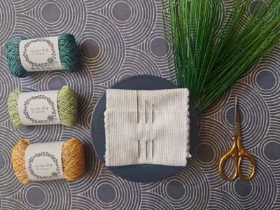 Was ist Sashiko? - Japanische Stickerei links - japanische Sashiko-Stickgarne, im HIntergrund japanischer Stoff, in der MitteSashiko-Sticknadeln, rechts -Stickschere