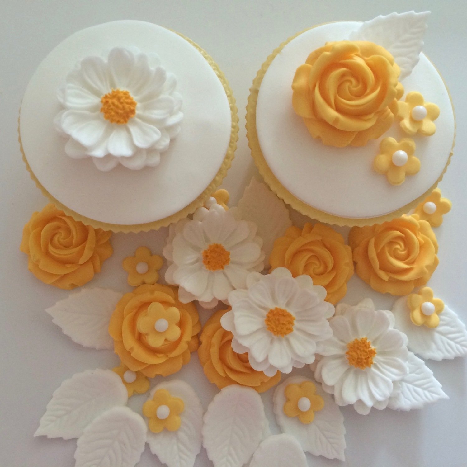 Apricot coloured roses, large hand-painted white daisy style flowers, small apricot coloured flowers with white sugar pearl centres, white leaves illustrated on two cupcakes.