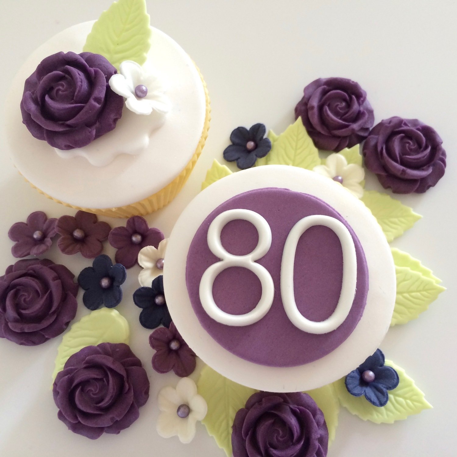 Purple 80 plaque with purple roses, pale green leaves and small flowers illustrated on cupcakes.