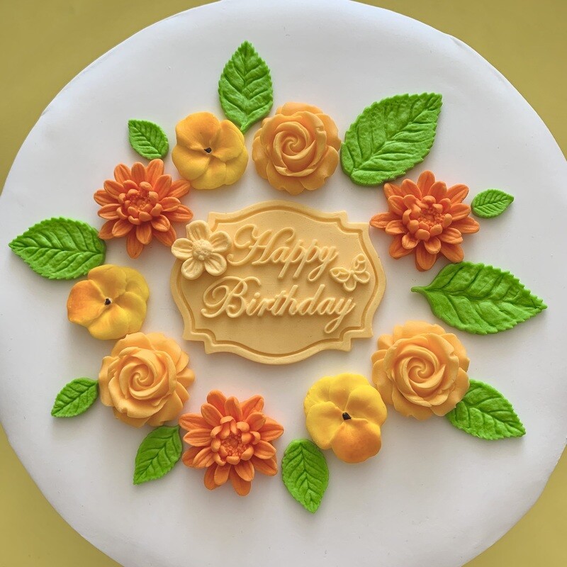 Apricot coloured Happy Birthday plaque with roses, dahlias, violas, green leaves.