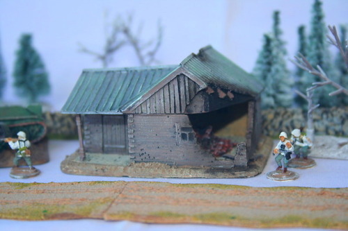 Battle-damaged L-shaped square log house, tin roof