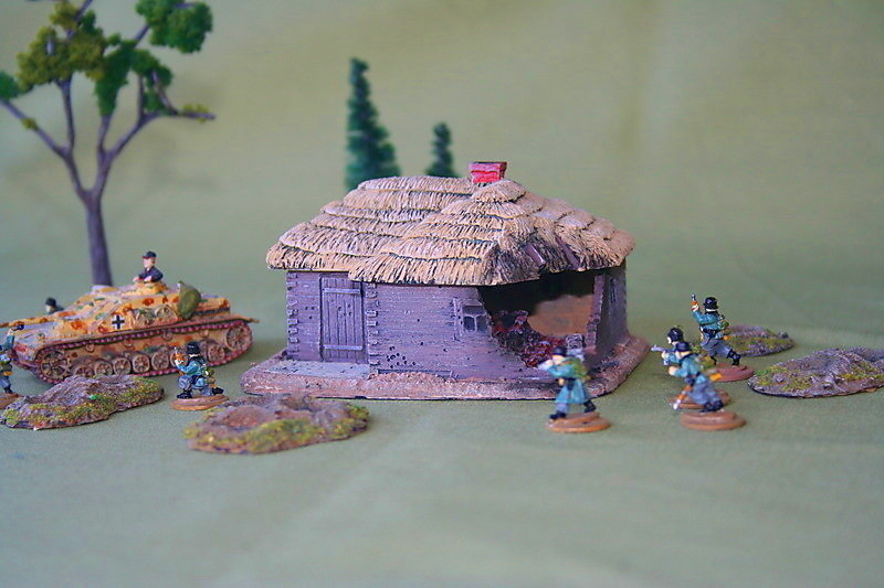 Battle-damaged L-shaped square log house, thatched roof