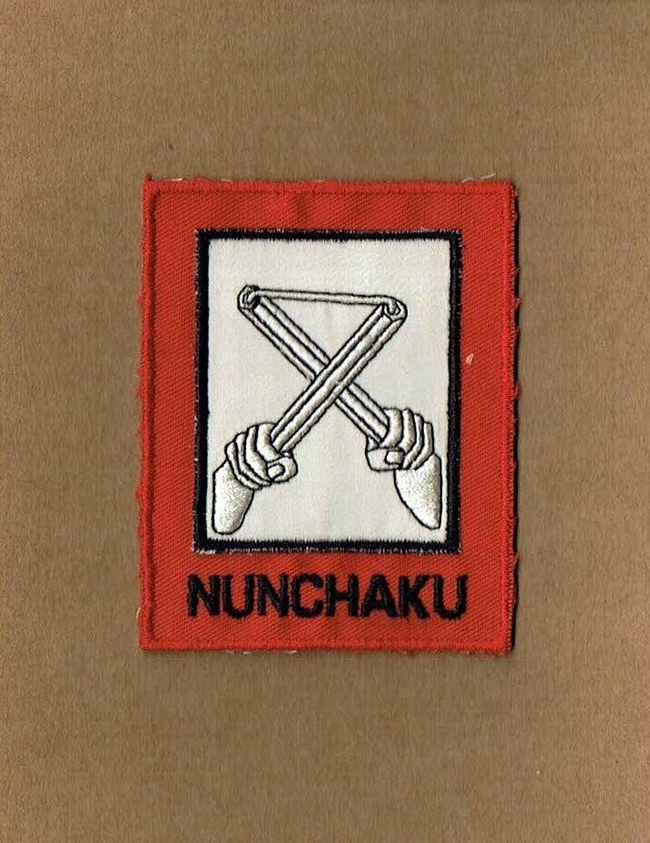 Patch/Écusson Broderie - Représentation de l'Arme "Nunchaku" en Blanc dans un Rectangle sous un Deuxième Rectangle  sous Fond Rouge  Écrit "Munchaku", Dimension  7 x 8.5 cm