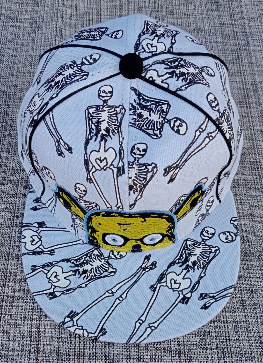 Une Casquette Blanc -Avec Impression de Squelettes de Couleur Blanc et Logo  " Demi Crâne Jaune".