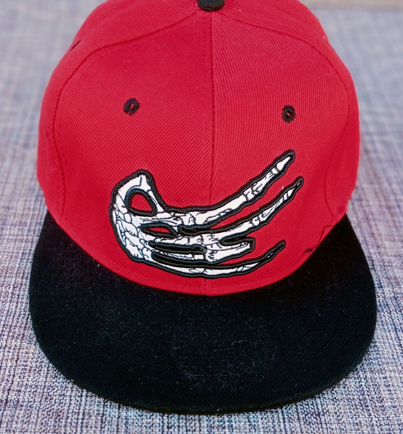 Une Casquette Rouge avec une Broderie "Main Squelette Blanc" et sa Visière Noire, de Style "Hit Hot" Broderie à l'Arrière.