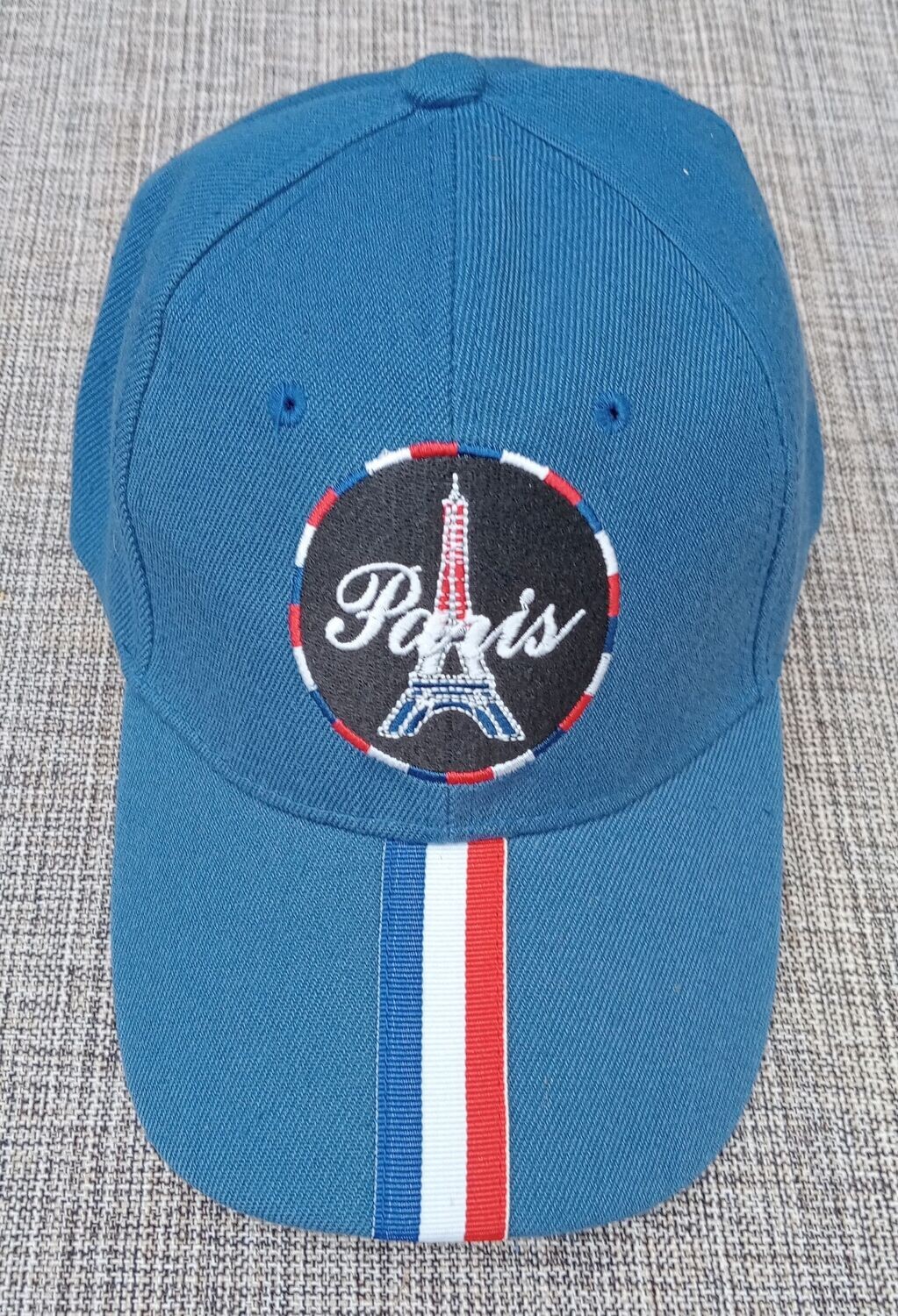 Une Casquette Bleu Marine avec une Broderie "Tour Eiffel, Paris" dans un Cercle Fond noir au Contour Couleur Française "BBR" et sur sa Visière Bombée une Bande au Couleur "Française"
