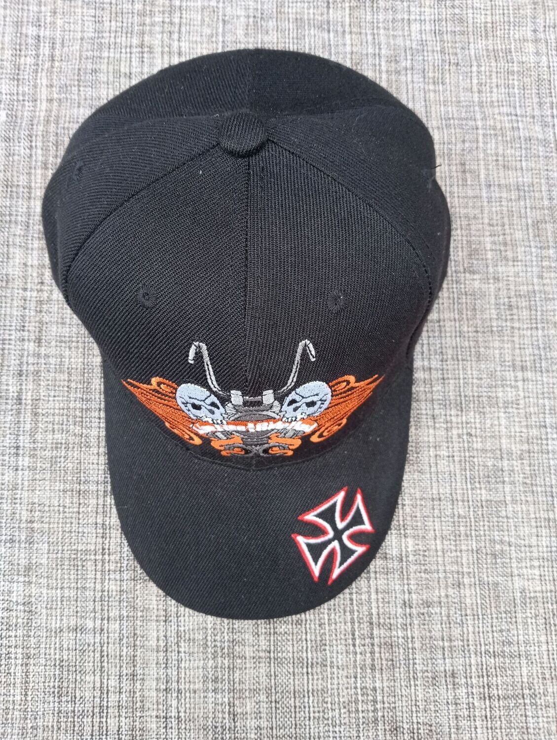 Une Casquette Noir avec une Broderie "Moto, 2 Crânes en Gris, Symbole Orange" et sur sa Visière Bombée Broderie "Croix Biker, Rouge/Blanc"