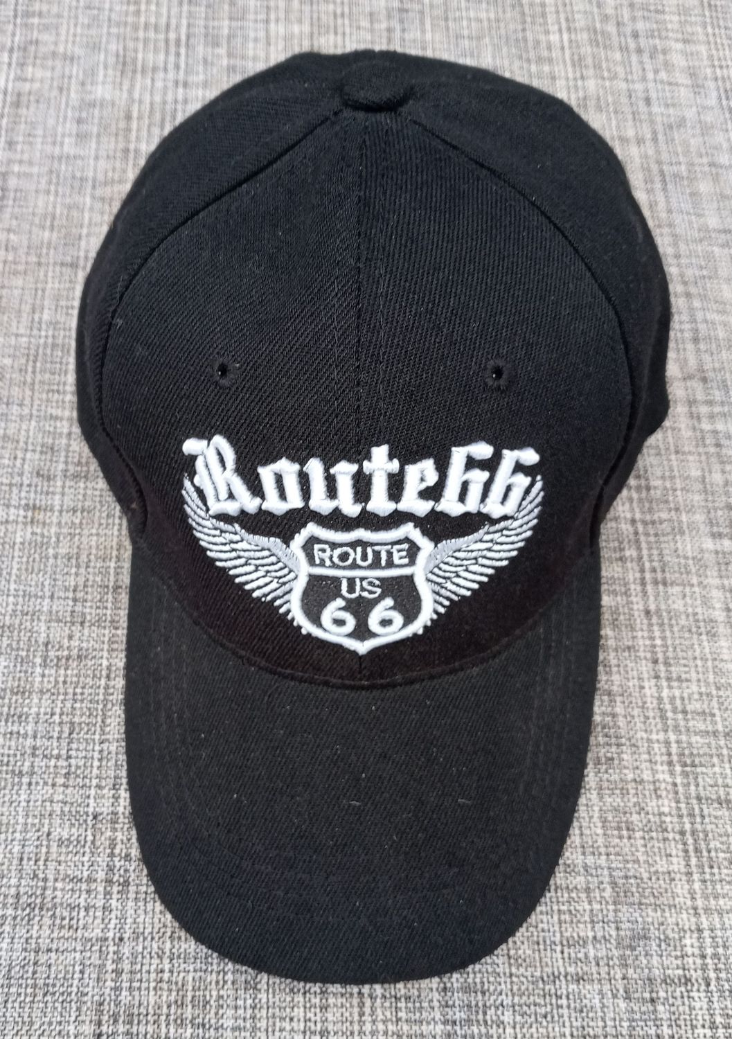 Une Casquette Noir avec une Broderie "Bouclier Route US 66, Route 66 Paire d'Aile en Blanc", et sa Visière Noire Bombée